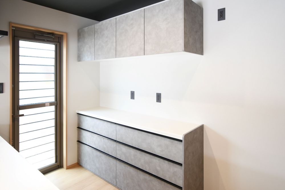 キッチン背面には、大容量のキャビネットを設置。引き出し収納と吊戸棚で、調理家電からストック品まですっきり整理整頓。生活感を隠しながら、空間を美しく保てます。※施工事例です。実物とは異なります。